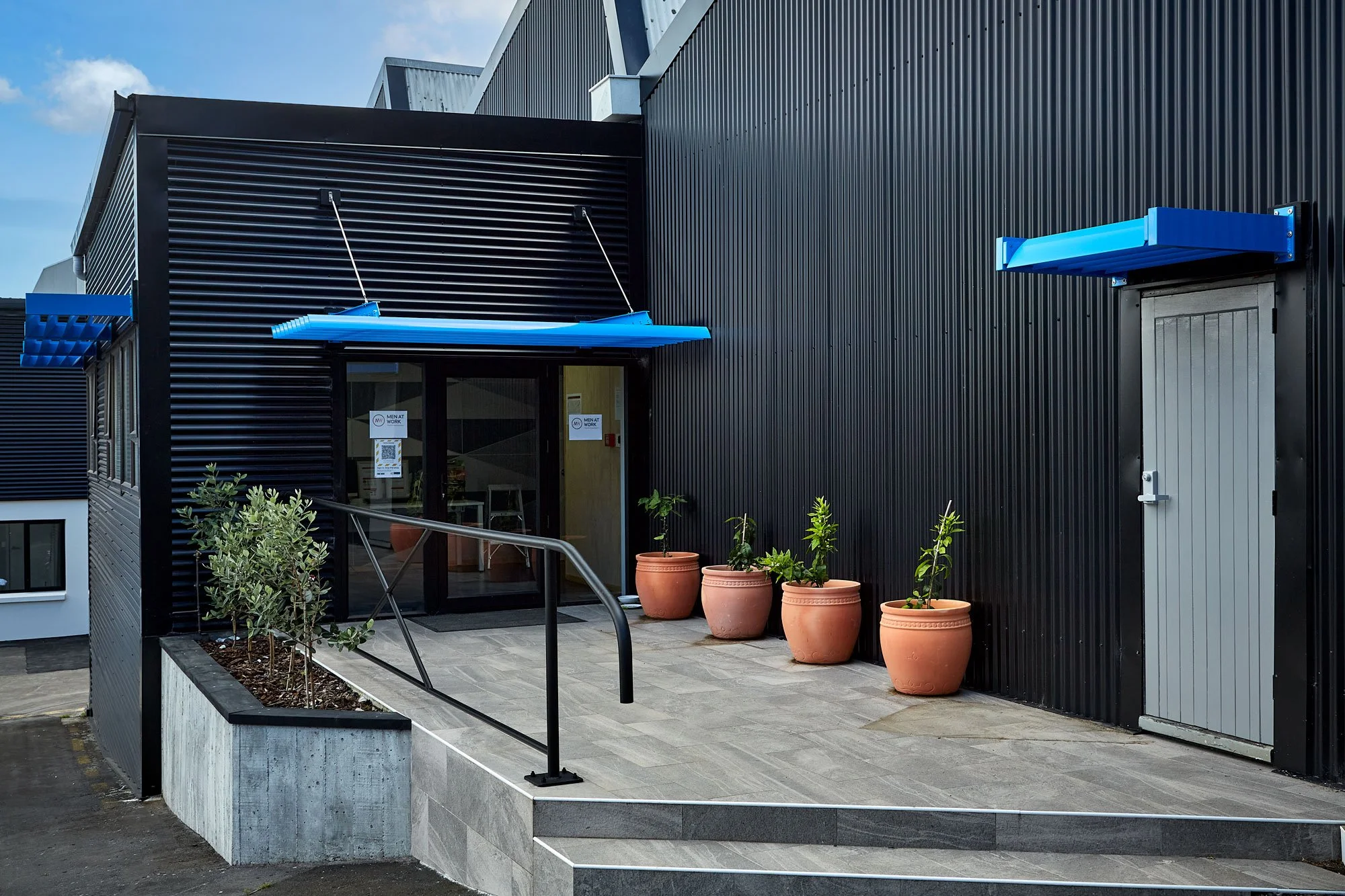 Main entrance with blue awning, tiled courtyard, and planter boxes