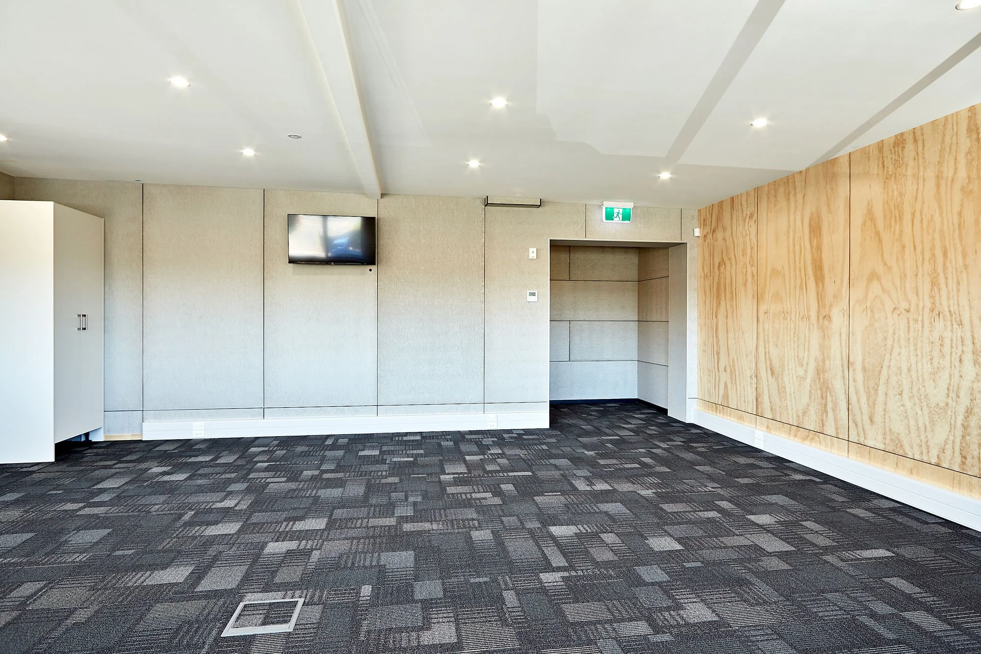 Meeting room with carpet tiles, plywood accent wall, and TV mount